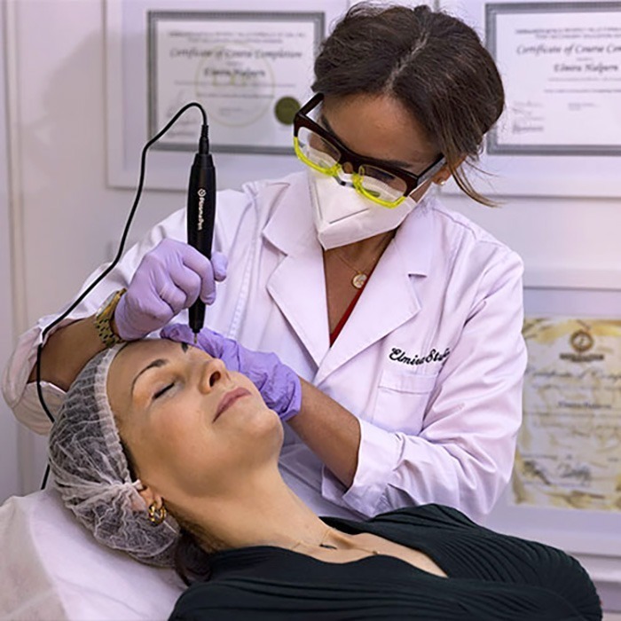 Elmira-plasma-pen-treatment-1-sq - Elmira Studio A woman is getting a facial treatment in a medical office.